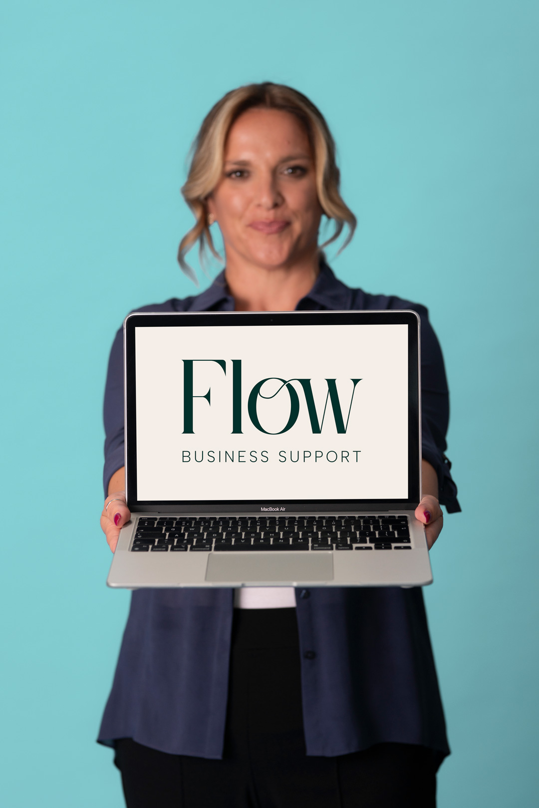 Michelle holding a laptop out in front of her with flow business support logo on the screen behind her is a light ocean blue background she's smiling