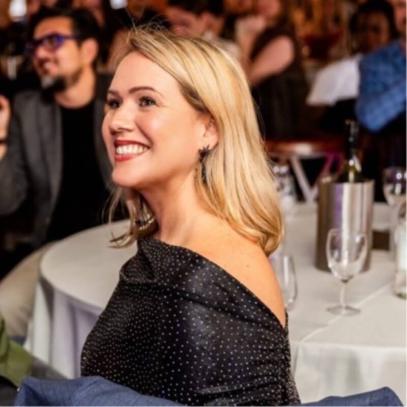 Lucy is smiling at an event in a black dress with blonde hair